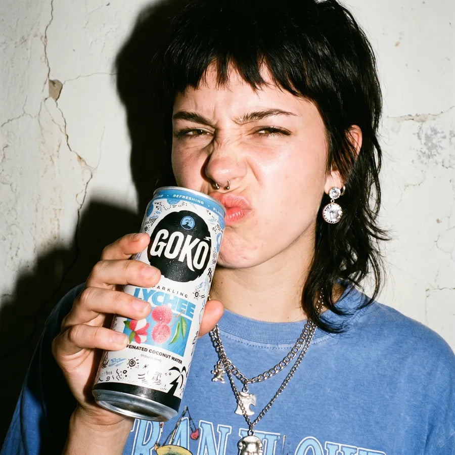 A woman pulling a face mid-sip of a GOKO Lychee can against a cracked wall